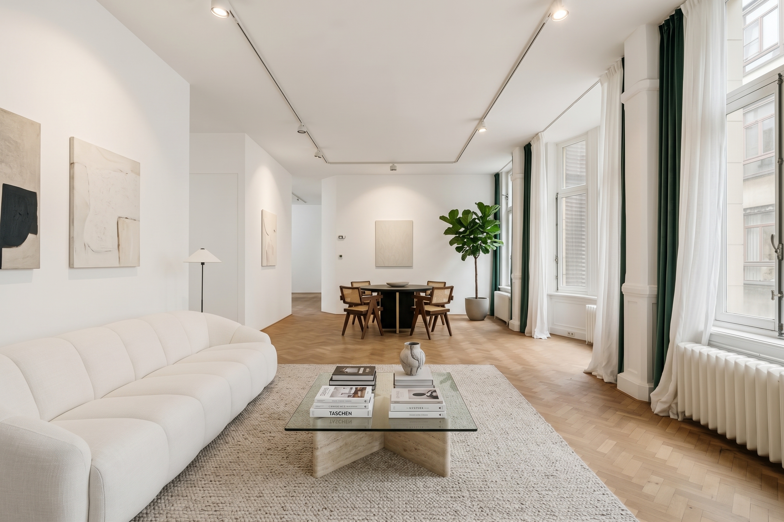 Modern living room with white sofa, glass coffee table, and dining area with wooden chairs on herringbone hardwood floors. [AI-generated text] [AI-modified]
