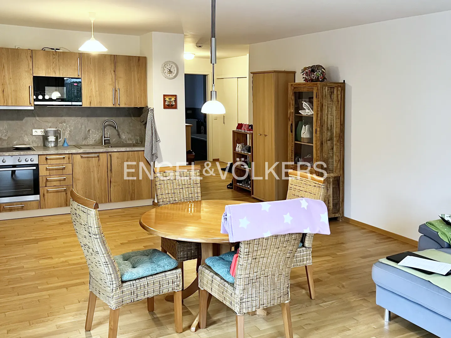 A bright, open-concept kitchen and dining area with wood floors, cabinets, and a round table with wicker chairs.