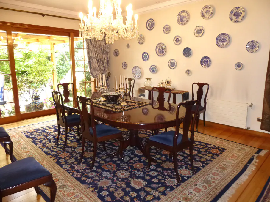 A formal dining room with a wood table, blue chairs, chandelier, and blue and white plates on the wall.