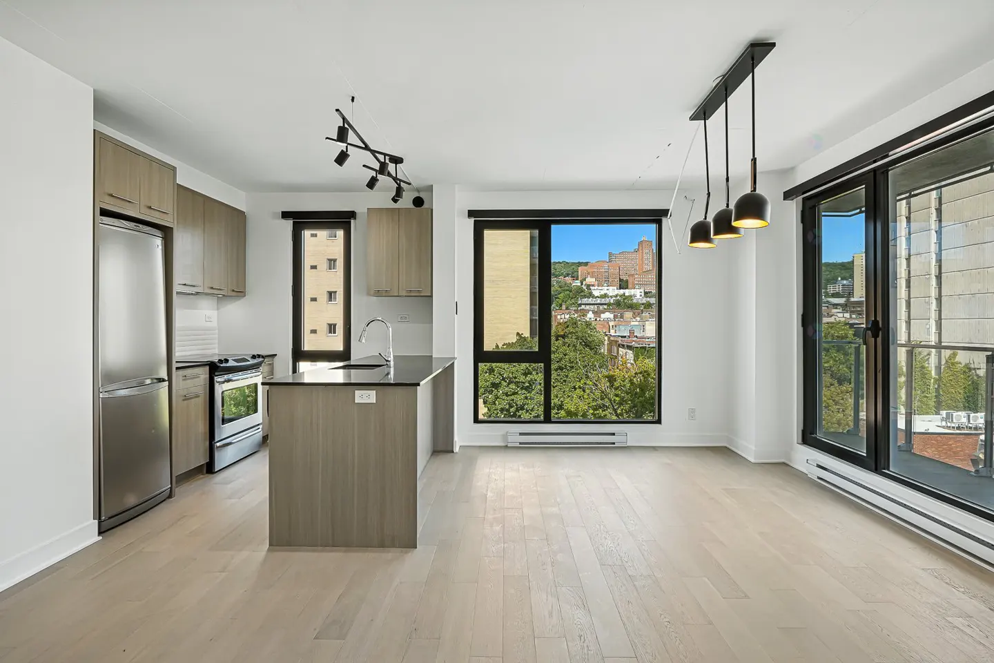Modern kitchen with light wood cabinets, stainless steel appliances, a kitchen island, and large windows with city views.