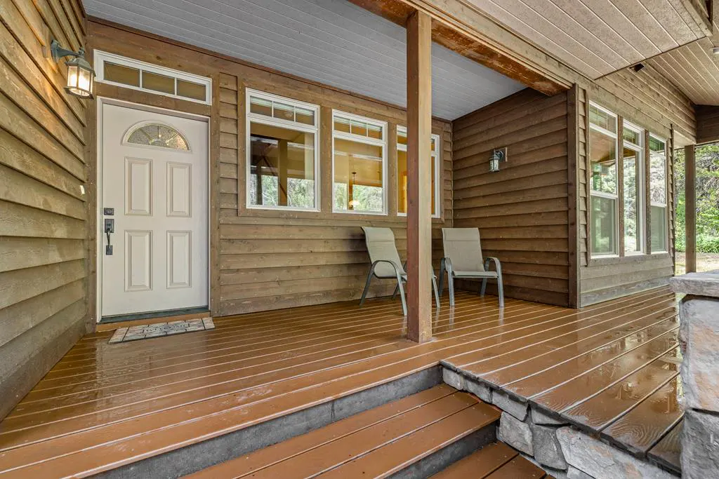 Covered porch with wood siding, a white front door, and two chairs. The porch floor is brown wood.