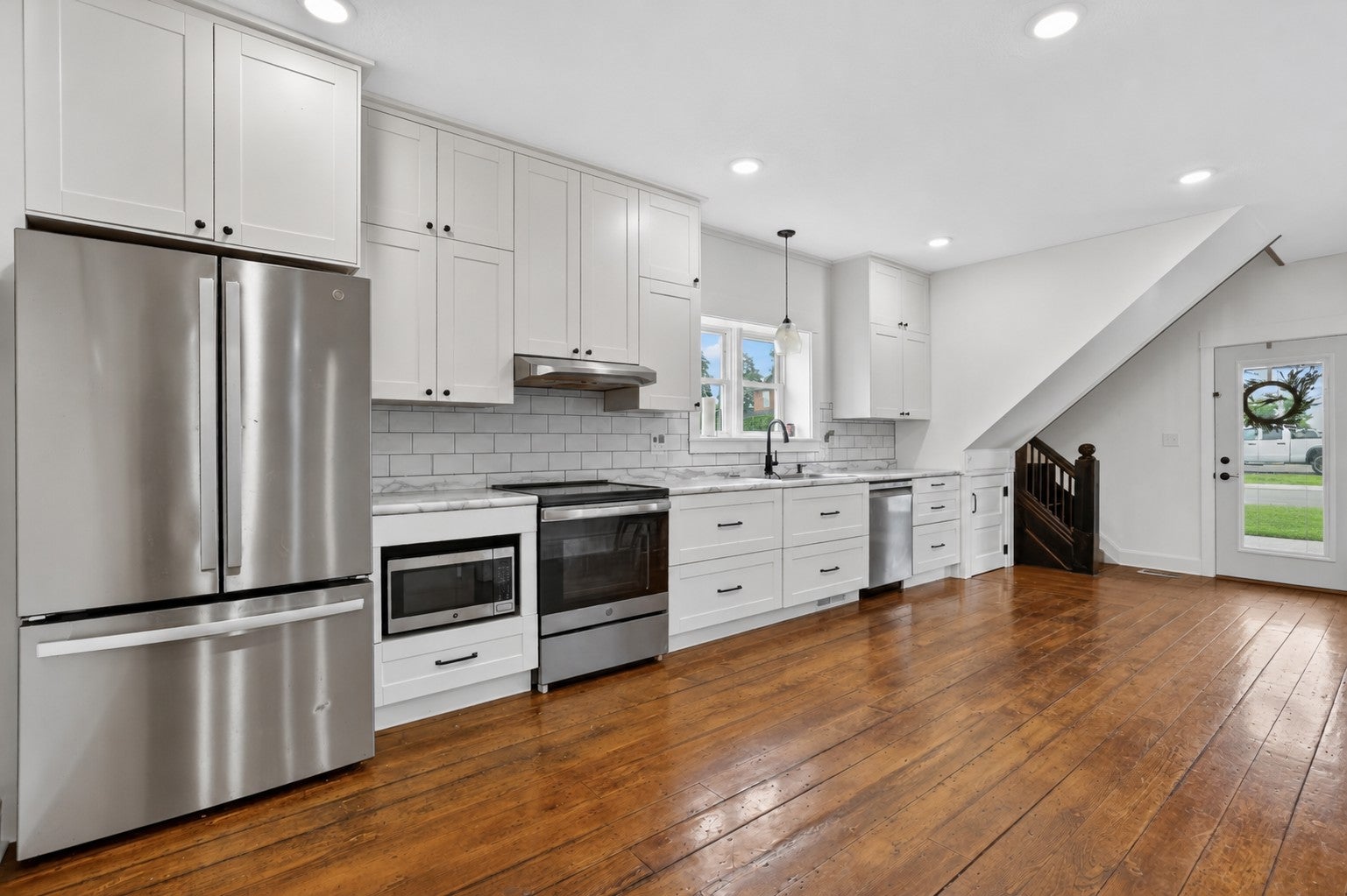 Modern kitchen with white cabinets, stainless steel appliances, subway tile backsplash, and hardwood floors. [AI-generated text]