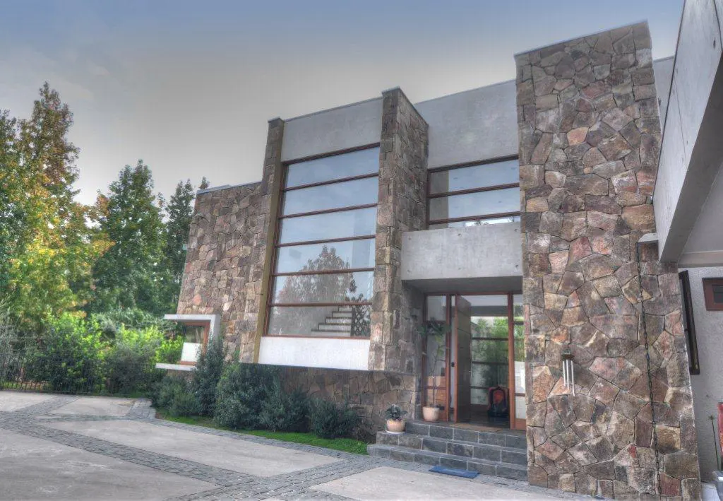 Modern home exterior with stone accents, large windows, and a gray driveway. Trees are visible in the background.