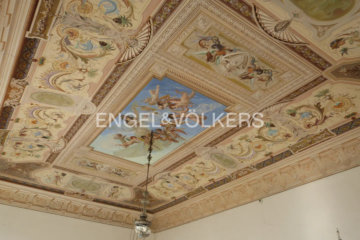 Ornate ceiling with painted cherubs and floral designs in pastel colors, framed by decorative molding. A chandelier hangs below.