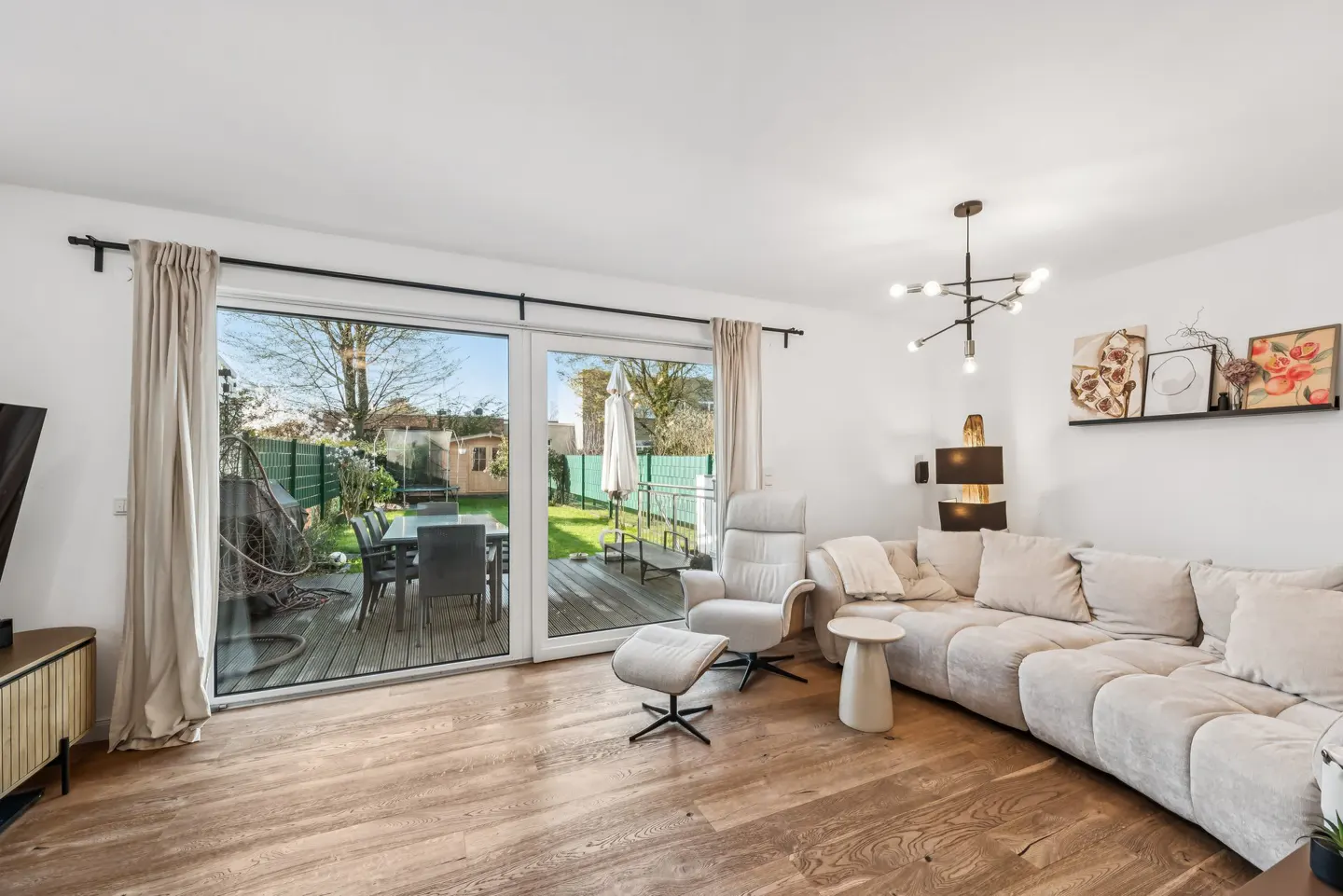 Bright living room with wood floors, a large beige sectional sofa, and a white recliner. Sliding glass doors open to a patio and green lawn.