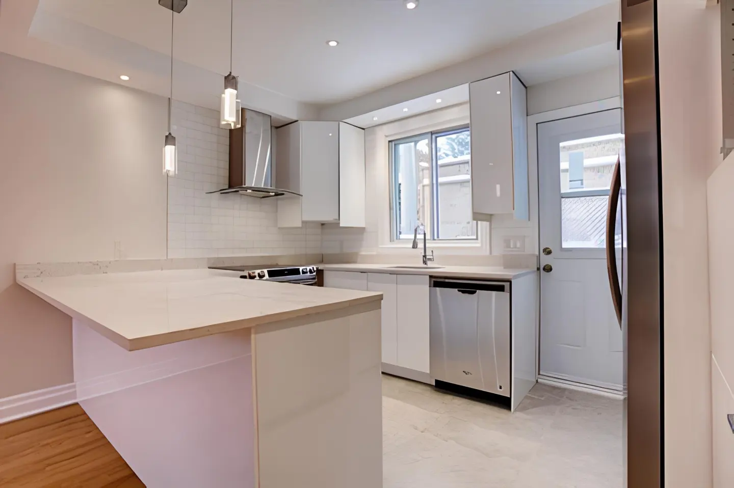 Modern kitchen with white cabinets, quartz countertops, stainless steel appliances, and a breakfast bar island.