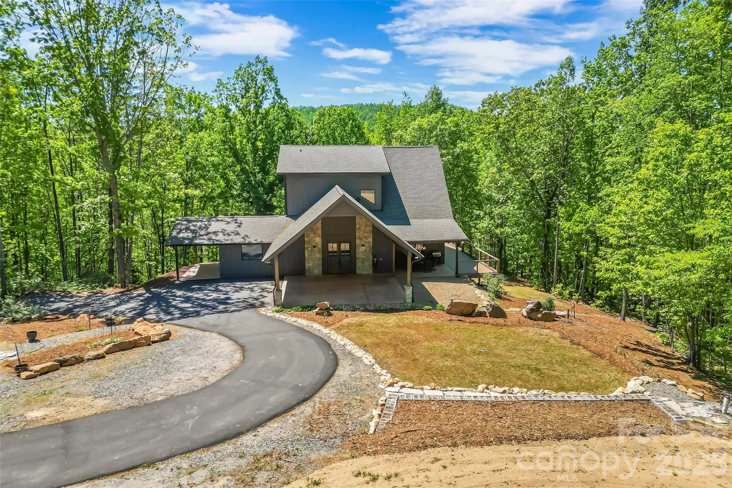 Gray two-story house with stone accents, a curved driveway, and surrounded by green trees.