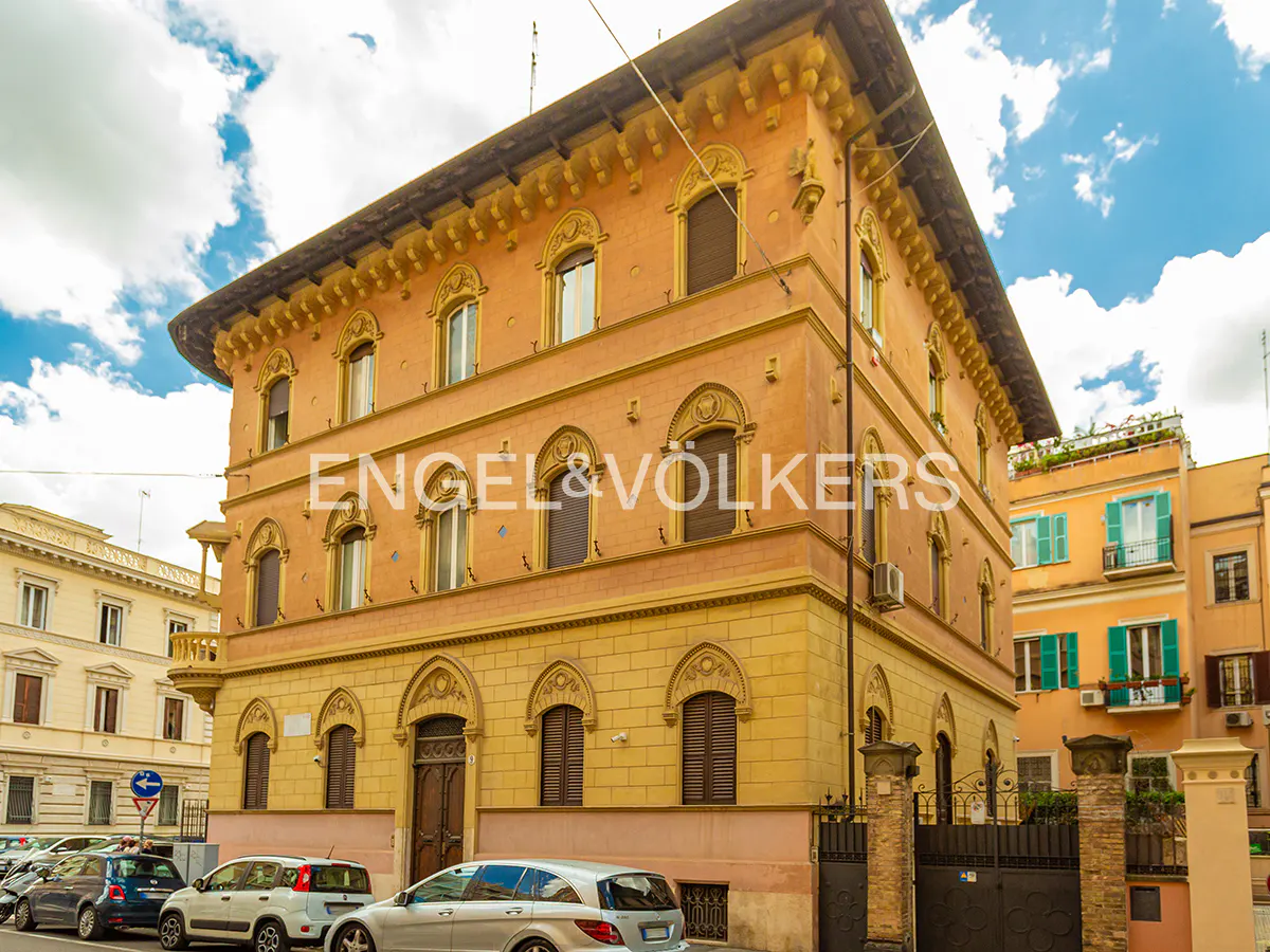 A multi-story, peach-colored historic building with arched windows and ornate detailing on a sunny city street.