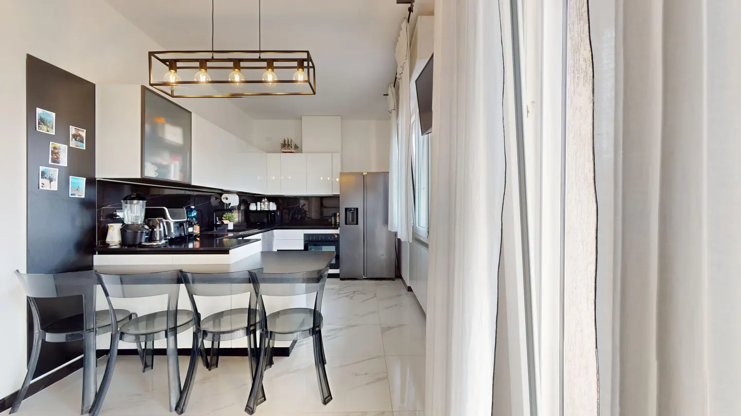Modern kitchen with white cabinets, black backsplash, stainless steel fridge, and four transparent chairs at a breakfast bar.