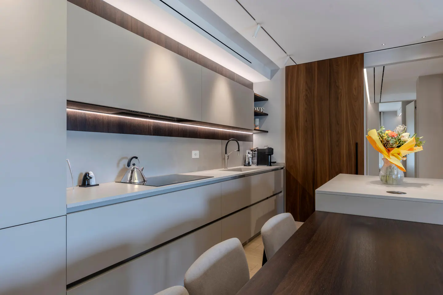 Modern kitchen with gray cabinets, wood accents, and a dark wood table. A bouquet of flowers sits on the island.