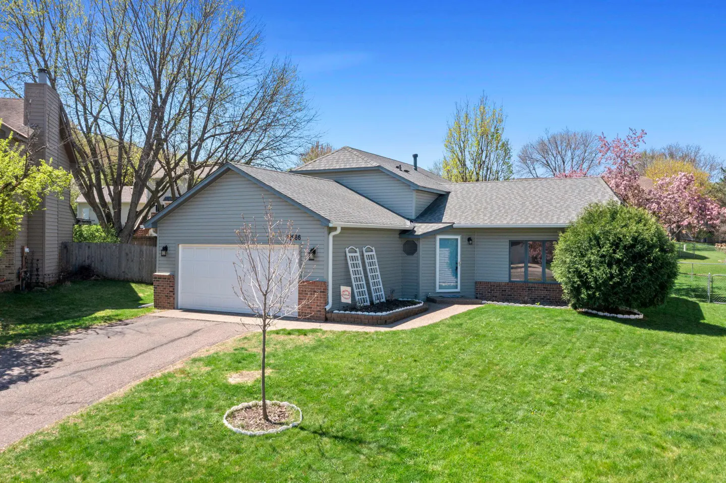 A single-story home with gray siding, a gray roof, and a white garage door sits on a green lawn under a blue sky.