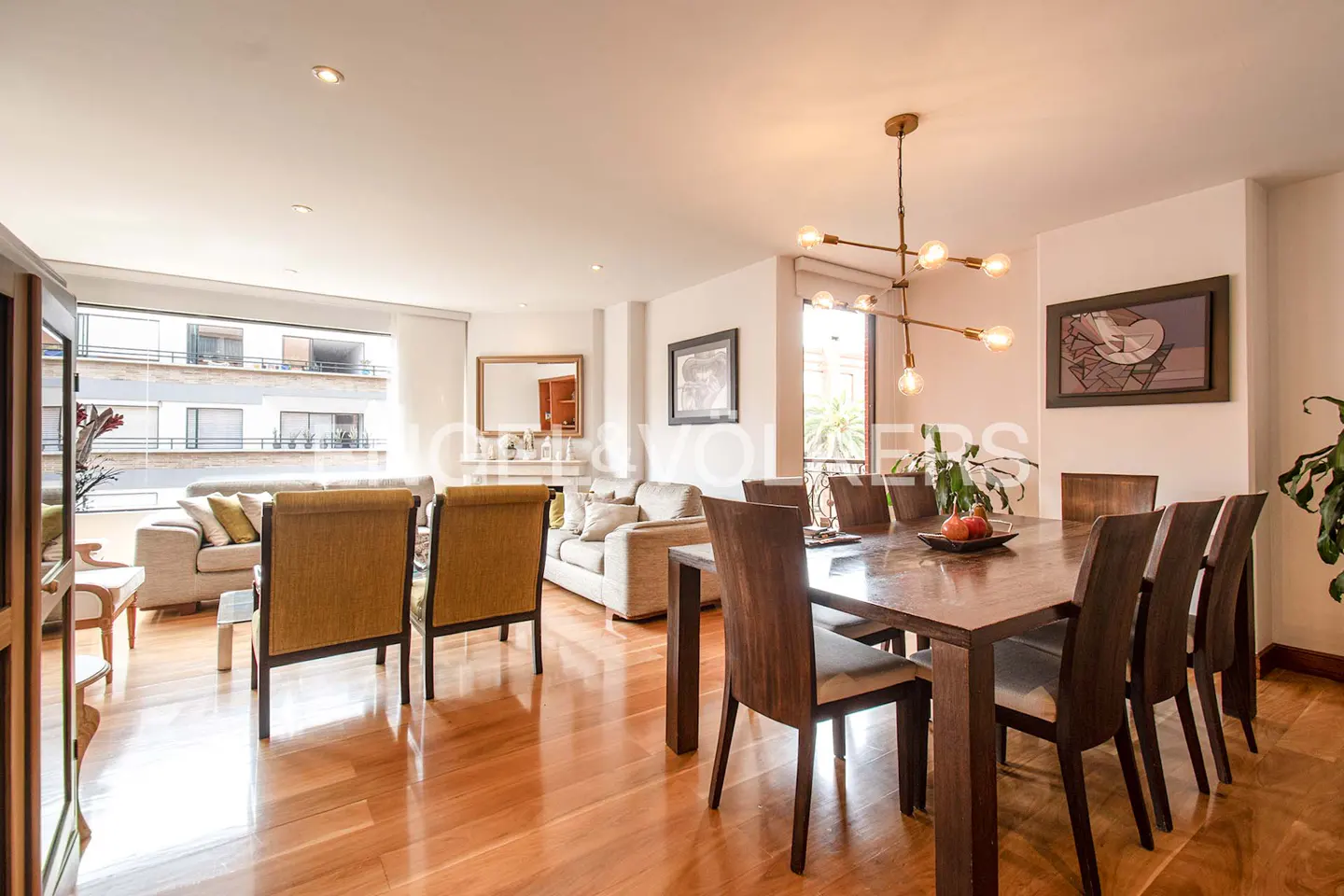 Bright open-concept living and dining area with hardwood floors, modern chandelier, and neutral-toned furniture.