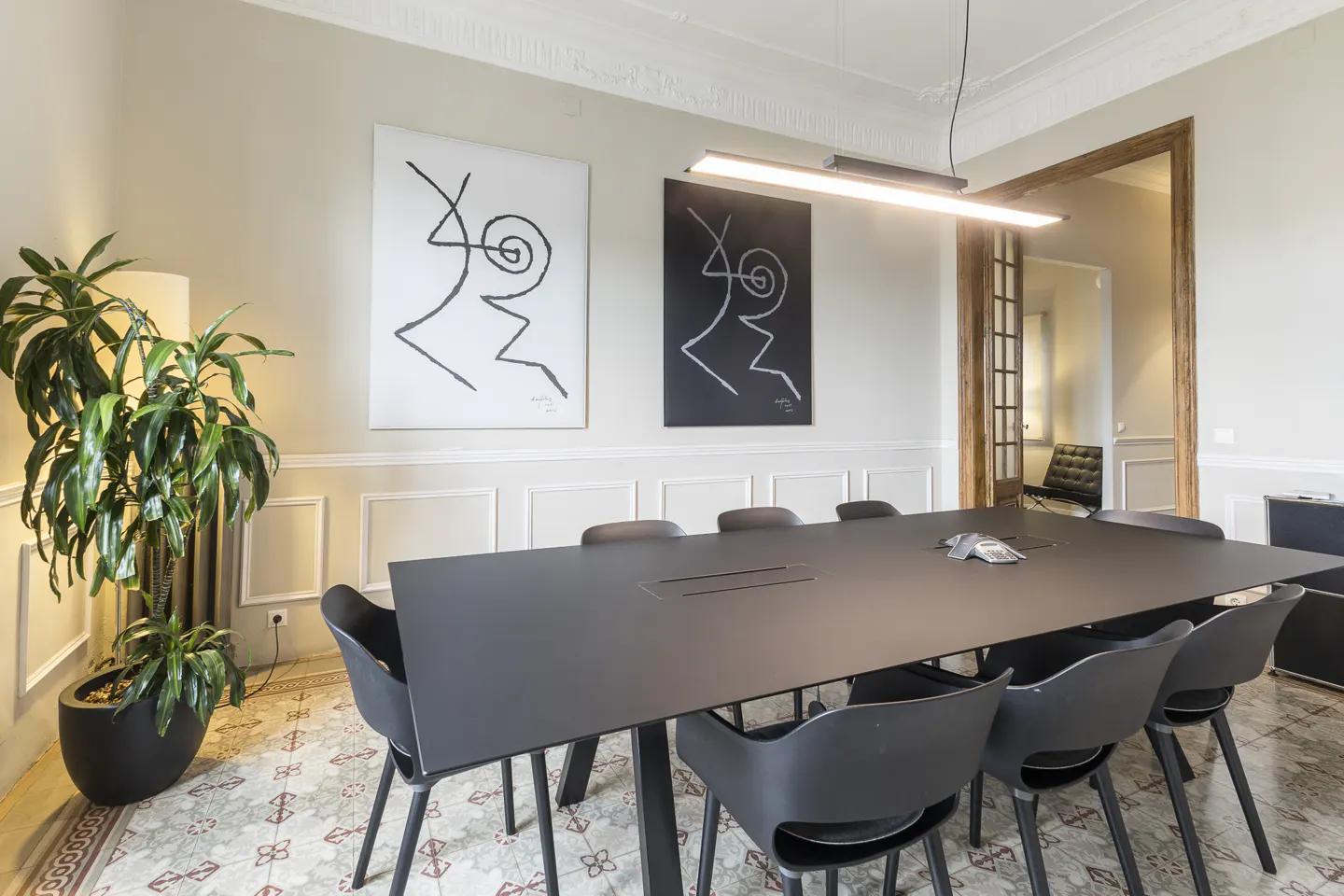 Modern conference room with a long black table, black chairs, patterned tile floor, and two abstract art pieces on the wall.