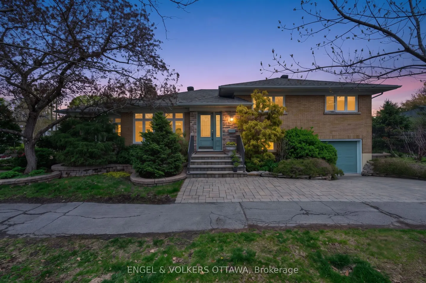 A single-family brick house with a blue door and garage, surrounded by trees and a stone walkway at dusk.