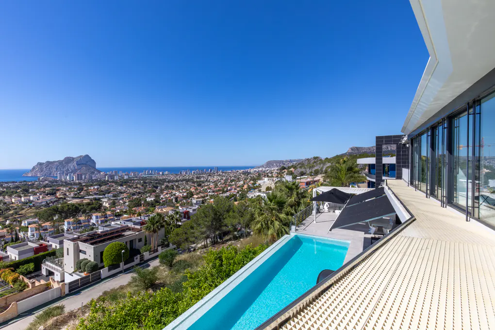 View from a modern villa with a blue pool overlooking a city by the sea under a clear blue sky.