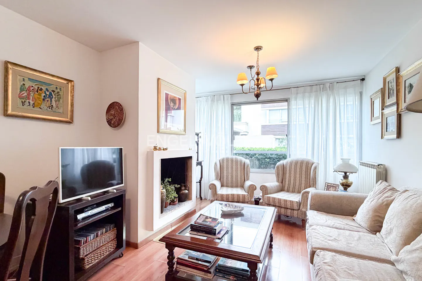 Living room with a beige sofa, striped armchairs, a fireplace, and a coffee table with books. A TV and dining table are also visible.