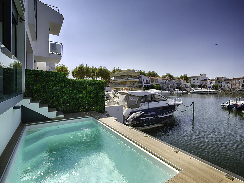A modern white house with a pool and a boat docked on a canal under a blue sky.