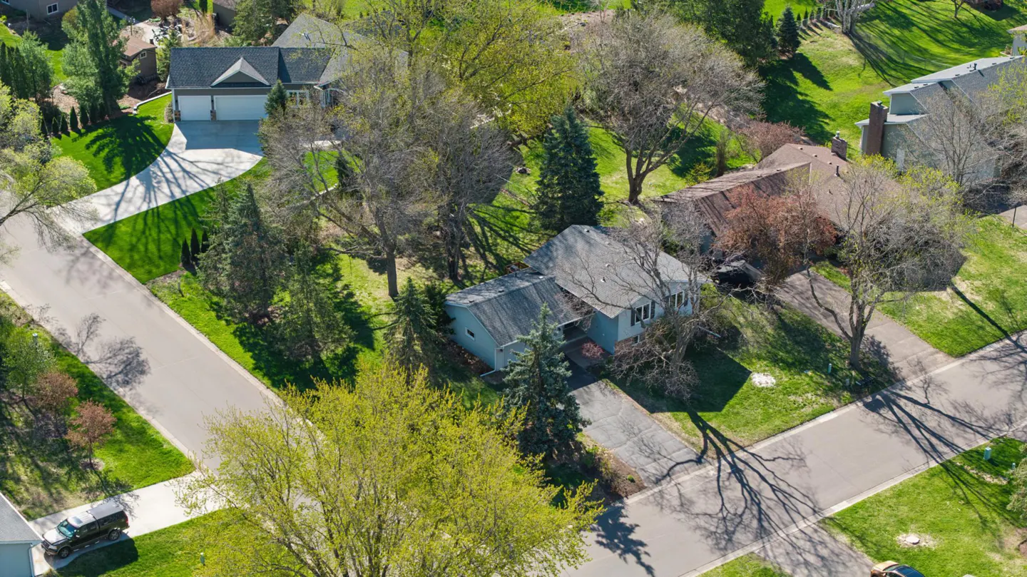 Aerial view of a residential neighborhood with houses, green lawns, trees, and paved roads on a sunny day.