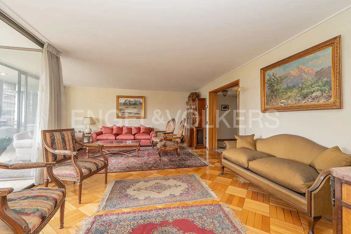 Living room with parquet floors, rugs, and antique furniture. A pink sofa and landscape paintings add color. Balcony view on the left.