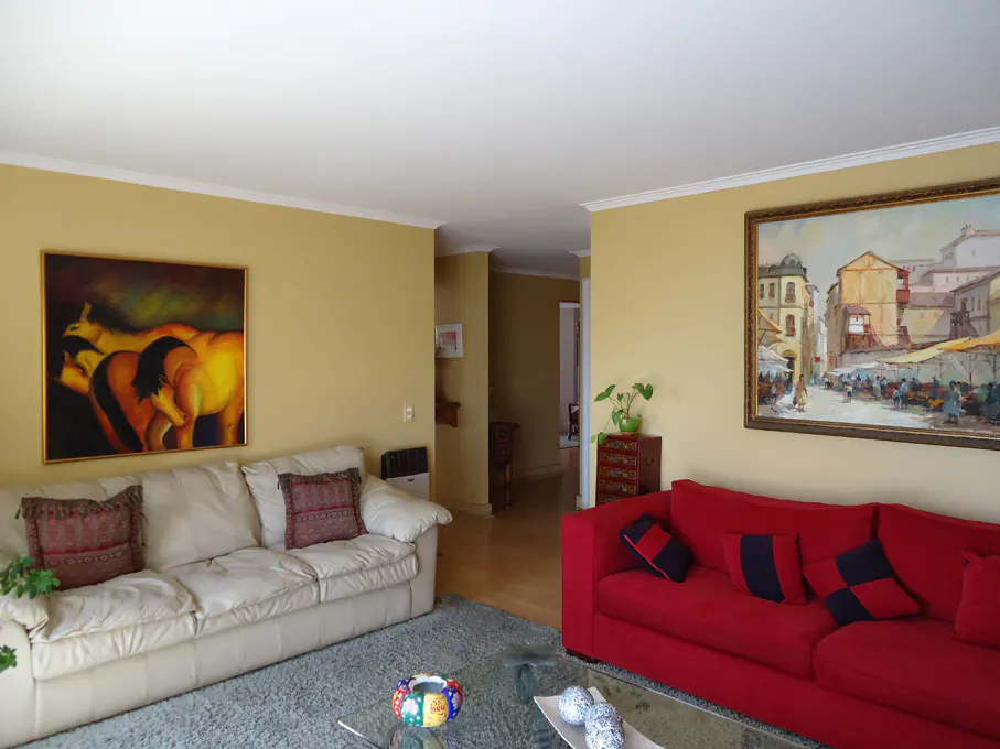 Living room with yellow walls, a white sofa with pillows, a red sofa with pillows, and paintings on the walls.
