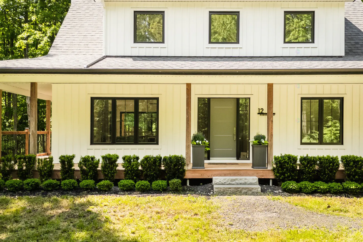 Exterior of a white farmhouse with black trim, a gray door, and green landscaping.