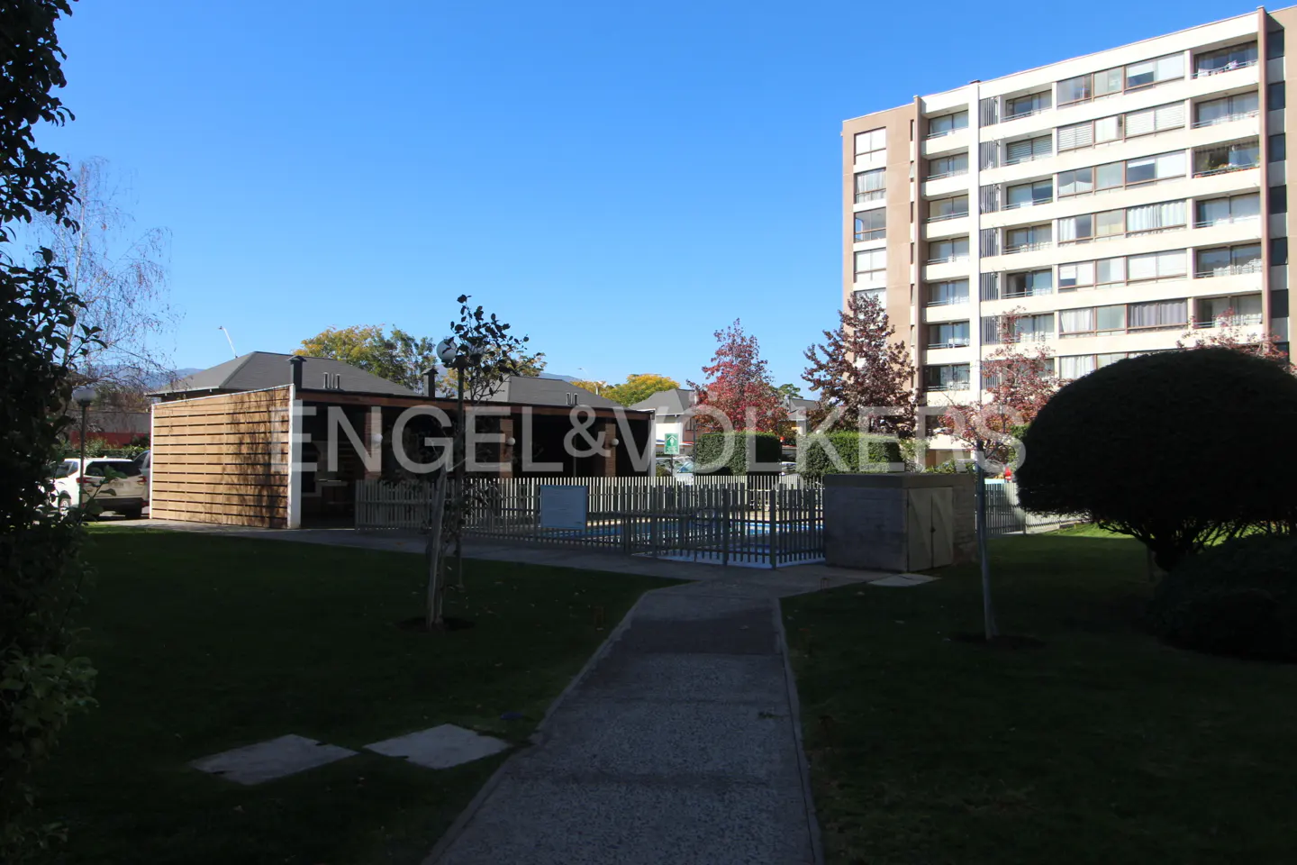 Exterior view of a tall apartment building with a pool area and the Engel & Volkers logo in the foreground.