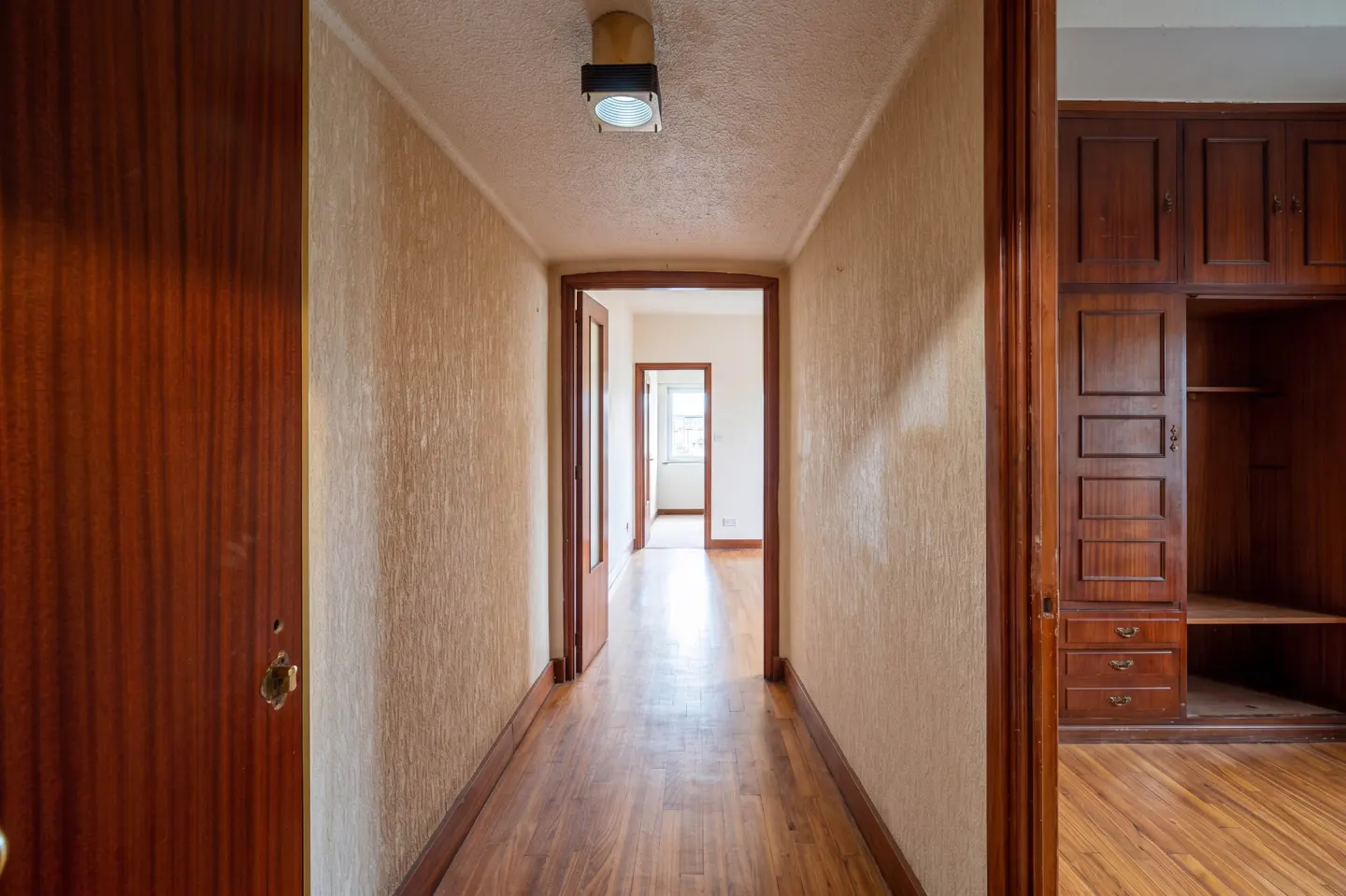 A long hallway with wood floors and textured beige walls leads to other rooms. A dark wood closet is on the right.