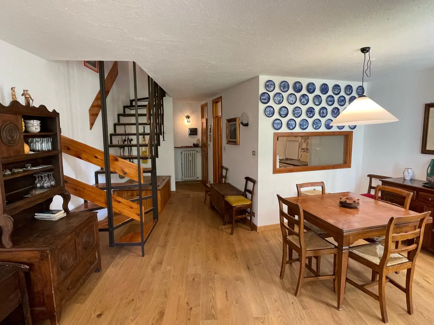 A bright, open-concept living and dining area with hardwood floors, a wooden dining table, and a staircase with black metal railings.