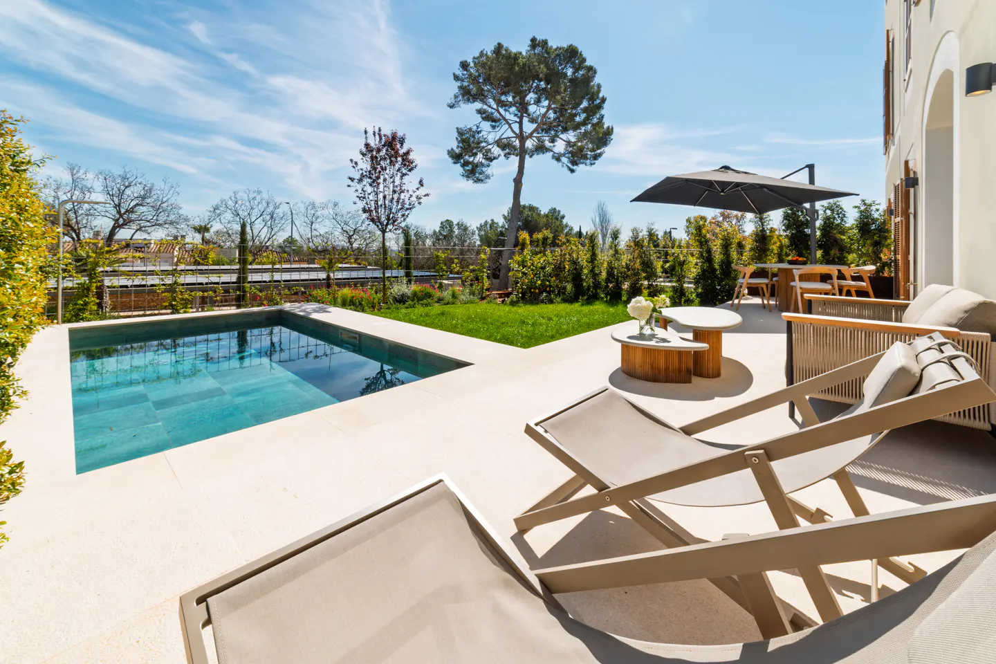 Outdoor patio with a pool, lounge chairs, and dining area under a black umbrella on a sunny day.