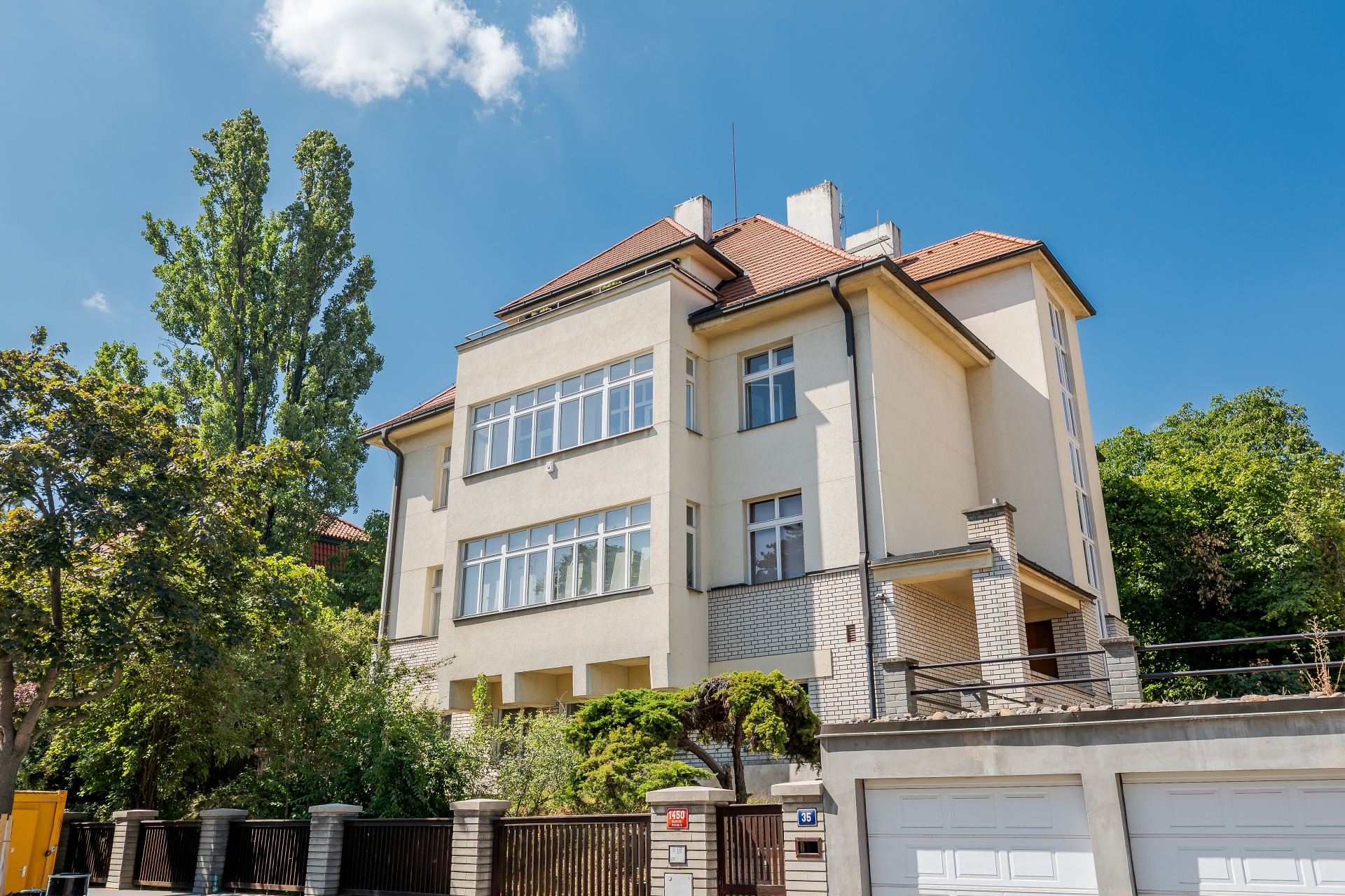 A three-story cream-colored villa with a red tile roof, large windows, and a brick base, set against a bright blue sky. [AI-generated text]