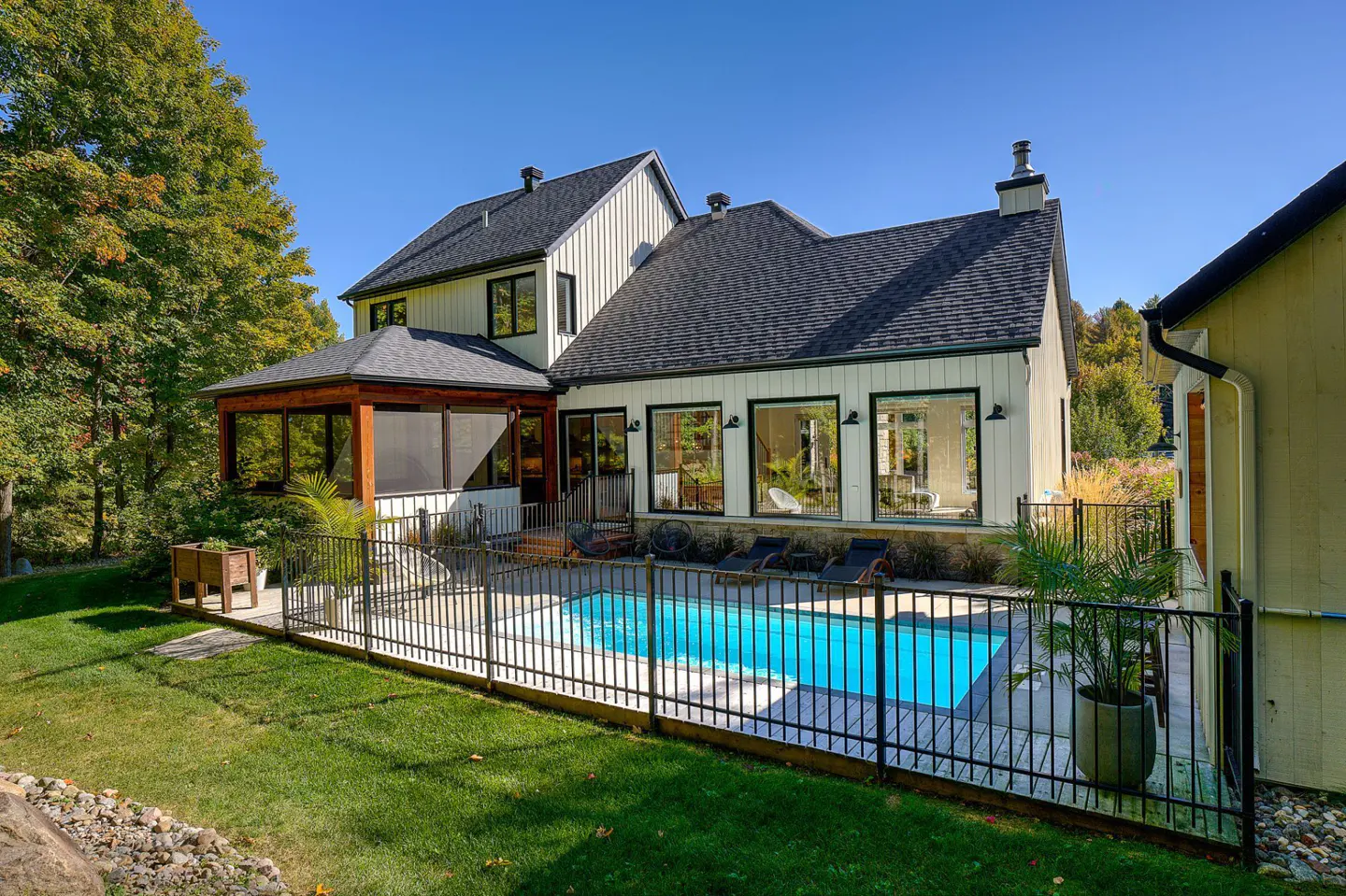 Backyard view of a two-story white house with a black roof, a pool, and a screened-in porch.