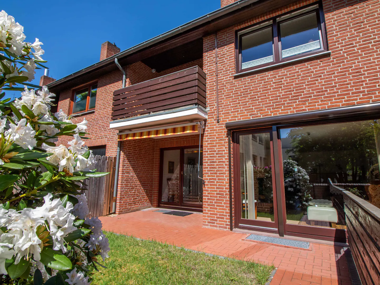 Exterior view of a two-story red brick house with a brown balcony and a patio with red brick flooring.