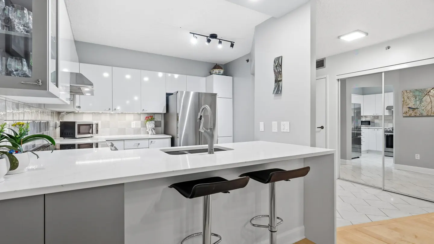 Bright kitchen with white cabinets, stainless steel appliances, and a white countertop island with two black bar stools.