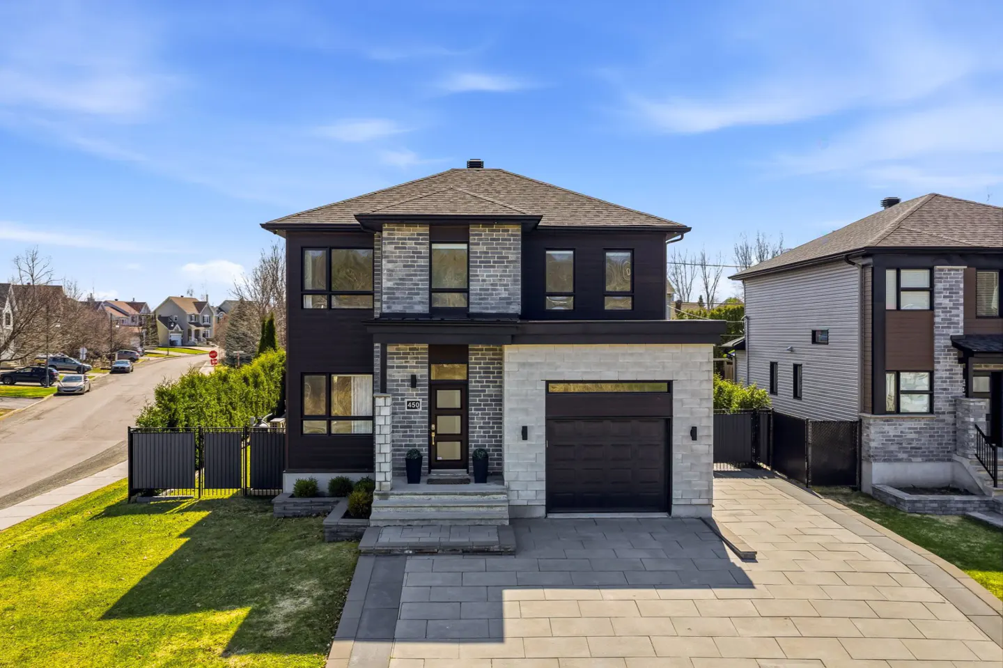 Two-story house with a gray brick and dark brown facade, a gray roof, and a black garage door. A gray stone driveway leads to the garage.