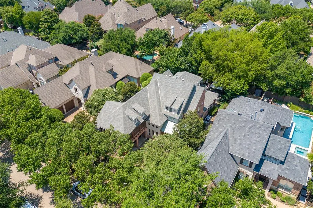 Aerial view of a residential neighborhood with large homes, green trees, and swimming pools.