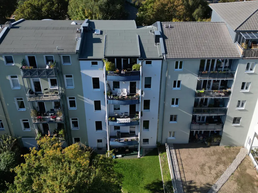 Aerial view of three apartment buildings with balconies, green trees, and a small lawn.