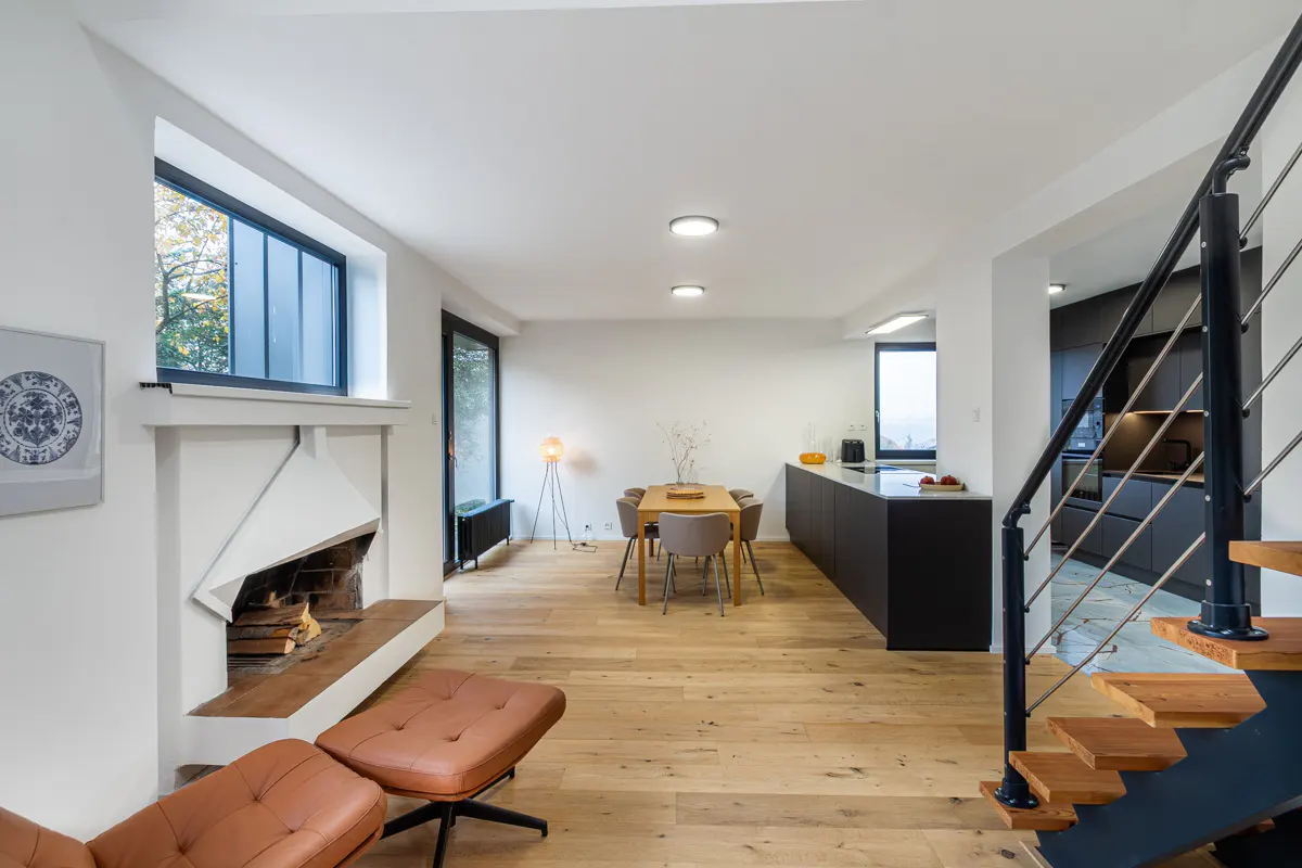 Open-concept living space with hardwood floors, fireplace, dining table, and black kitchen island. Staircase with metal railing on the right.