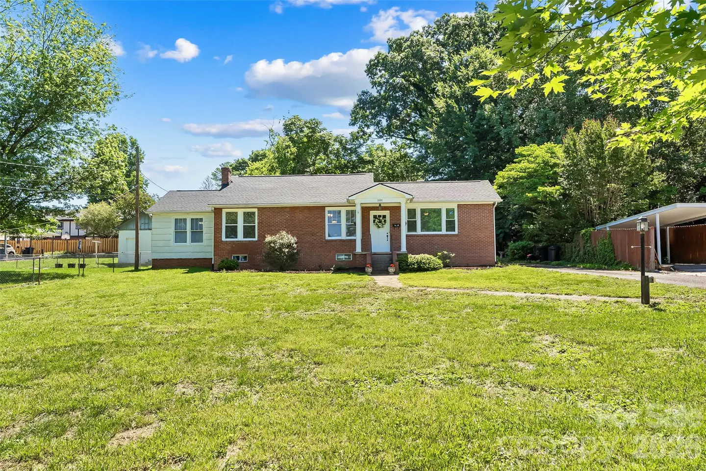 Single-story red brick ranch house with white trim, a front porch, and a large grassy yard under a blue sky.