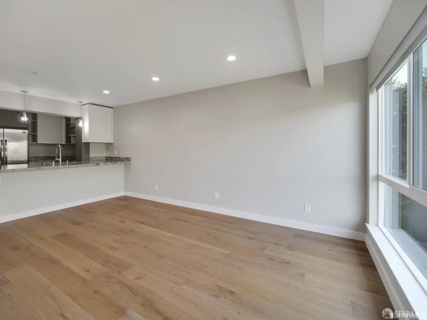 Bright, open-concept living space with wood floors, gray walls, and a modern kitchen with stainless steel appliances. Large window provides natural light.