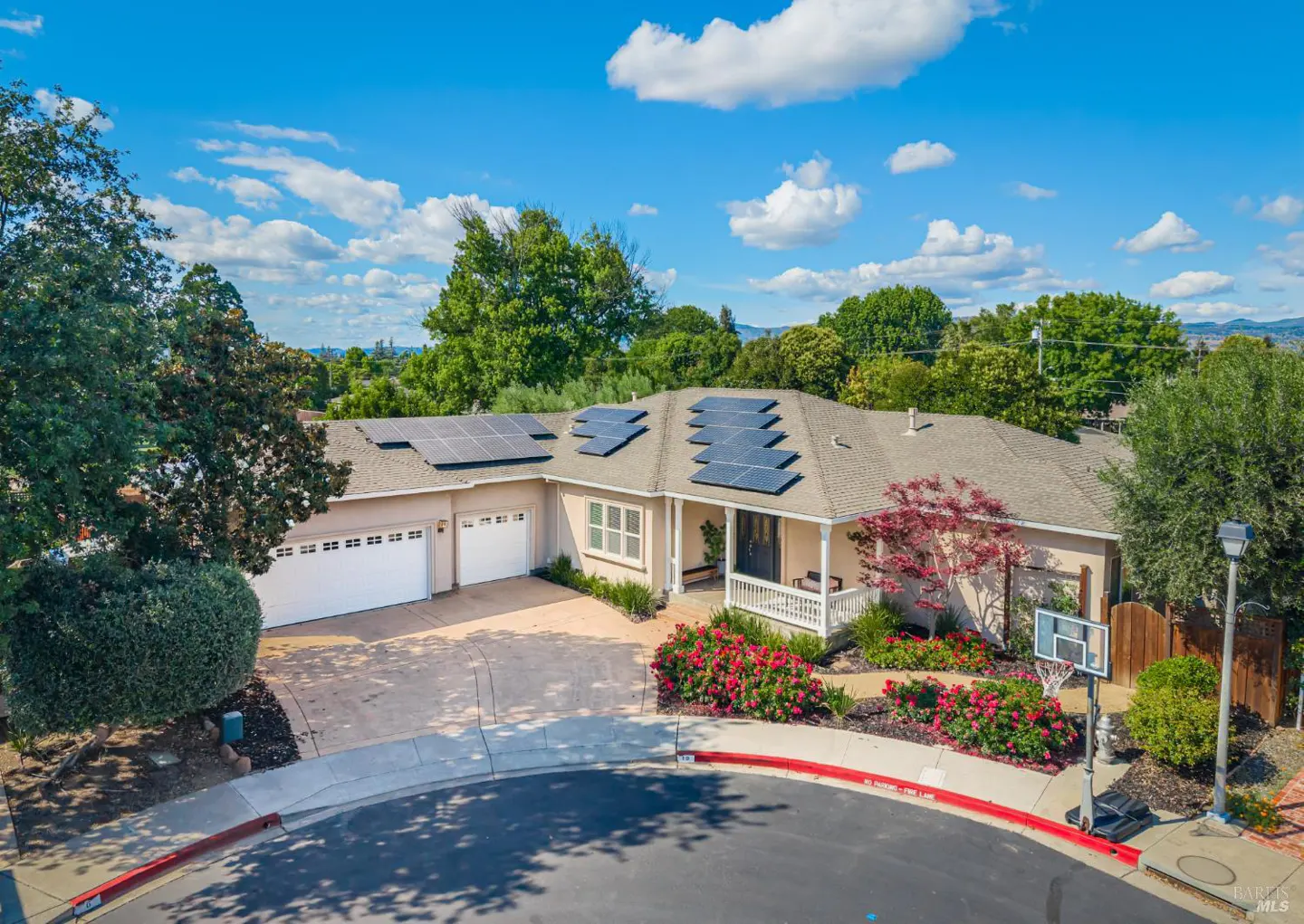 Single-story suburban home with solar panels, a three-car garage, and a front yard with blooming red flowers.