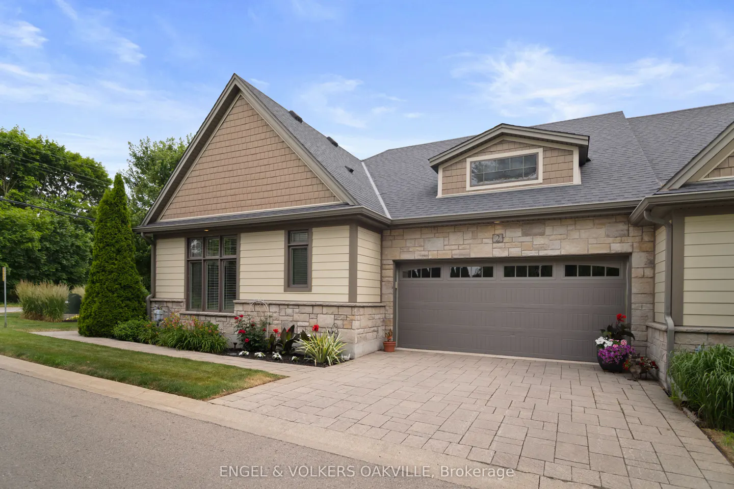 Exterior of a beige and stone house with a gray garage door and brick driveway.