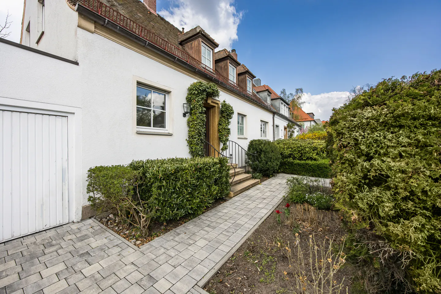 Exterior view of a white house with a stone walkway, green bushes, and a wooden door with ivy.