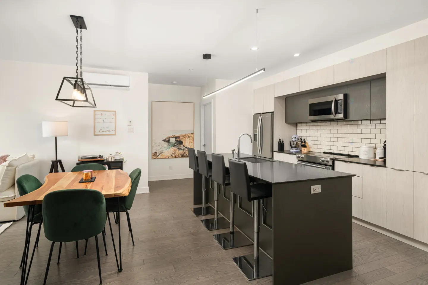 Modern open-concept kitchen with a dark island, bar stools, and a dining area featuring a live-edge wood table.