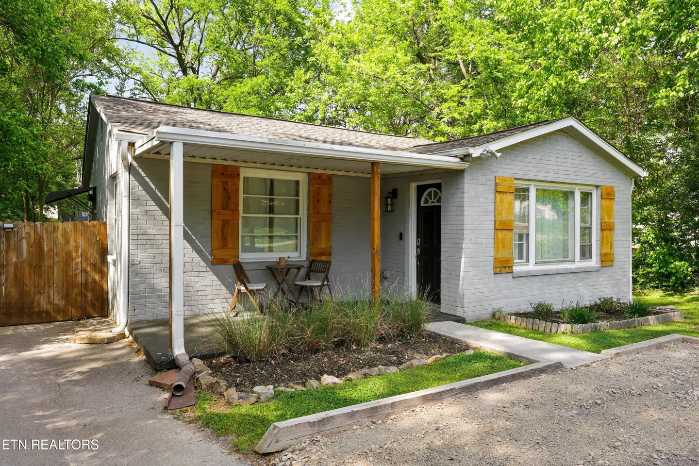 Exterior of a gray brick house with wooden shutters and a small porch with chairs.