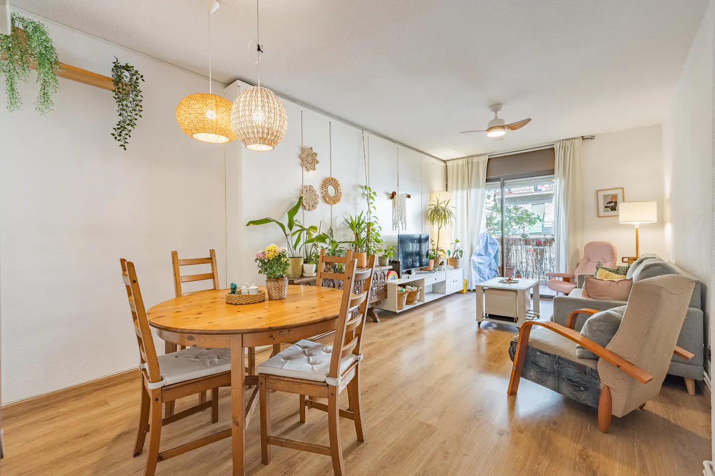 Bright living room with wood floors, a round table with four chairs, and a sofa. Plants decorate the room.