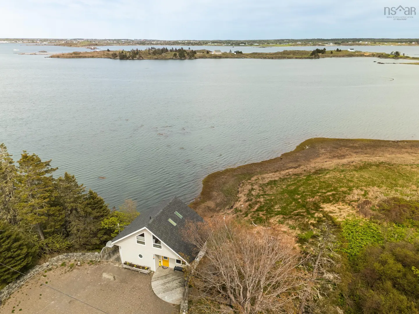 Aerial view of a white house with a yellow door, near water and islands.