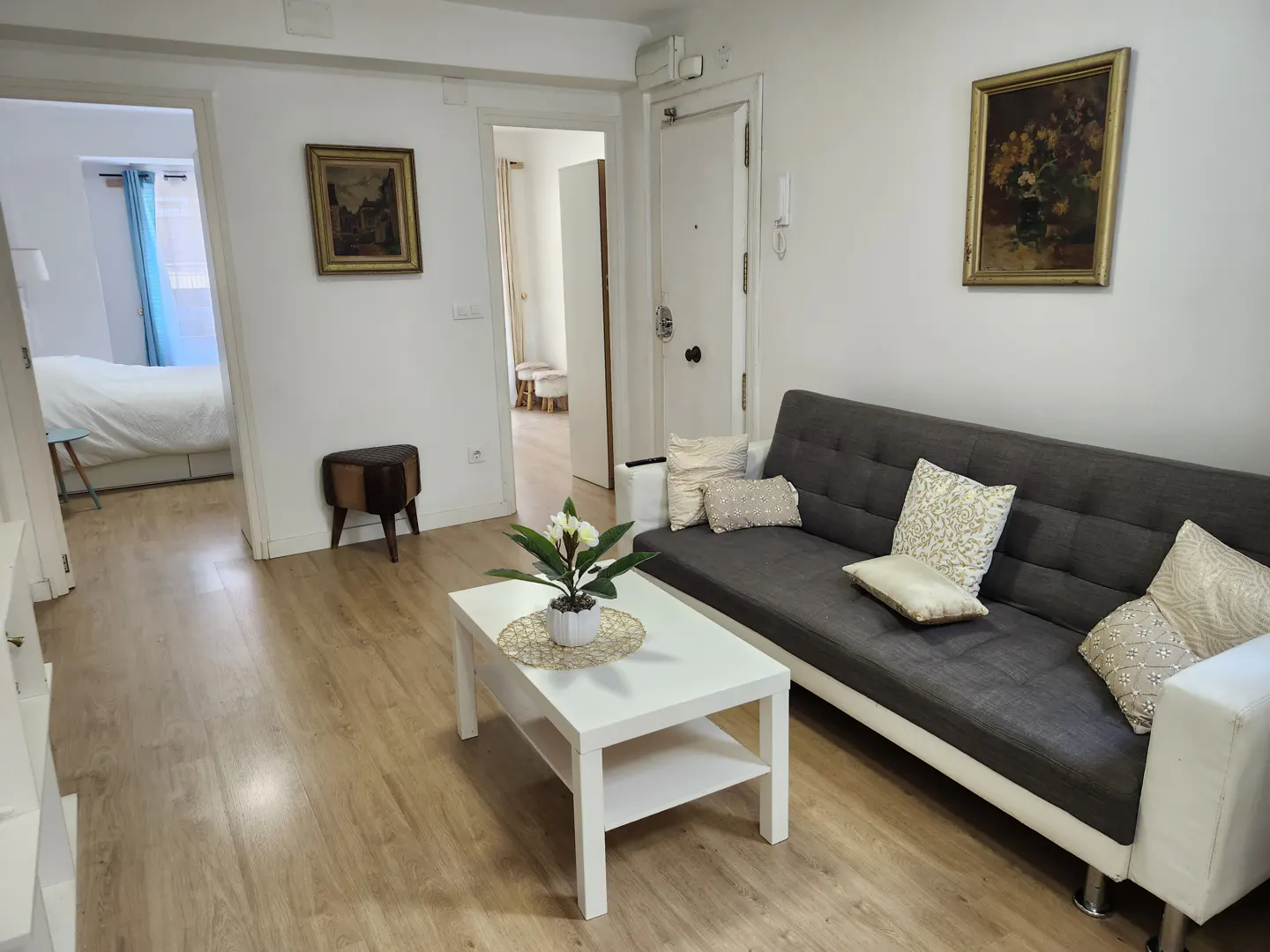 Living room with a grey sofa, white coffee table with a flower centerpiece, and doorways leading to other rooms.