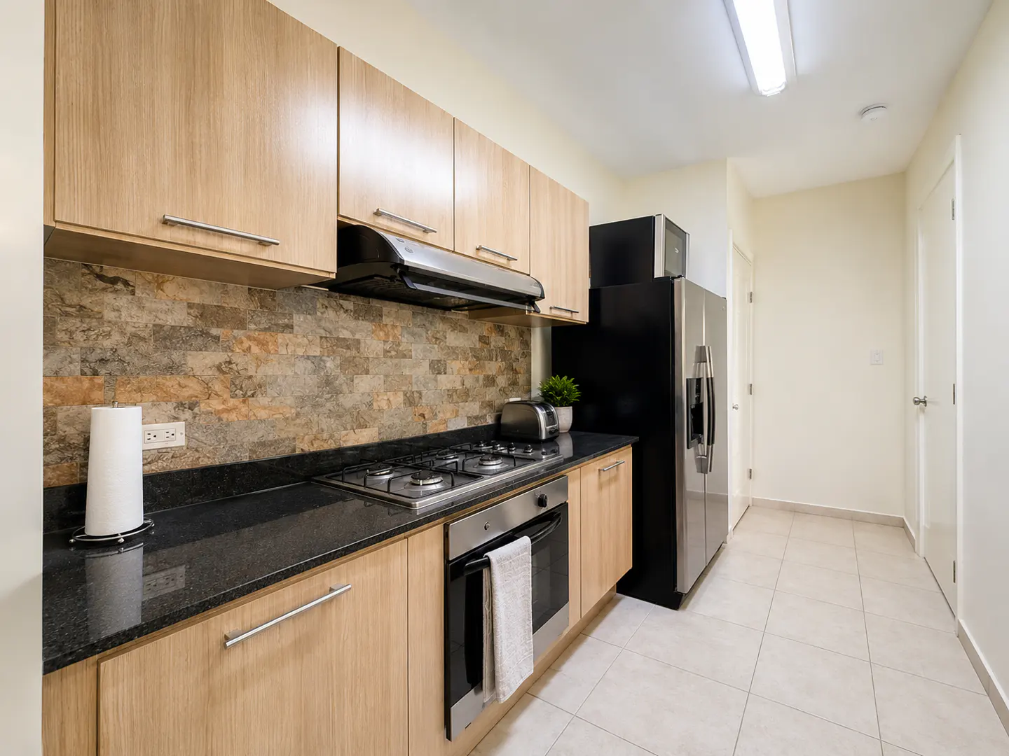 Modern kitchen with light wood cabinets, black granite countertops, stone backsplash, and stainless steel appliances.