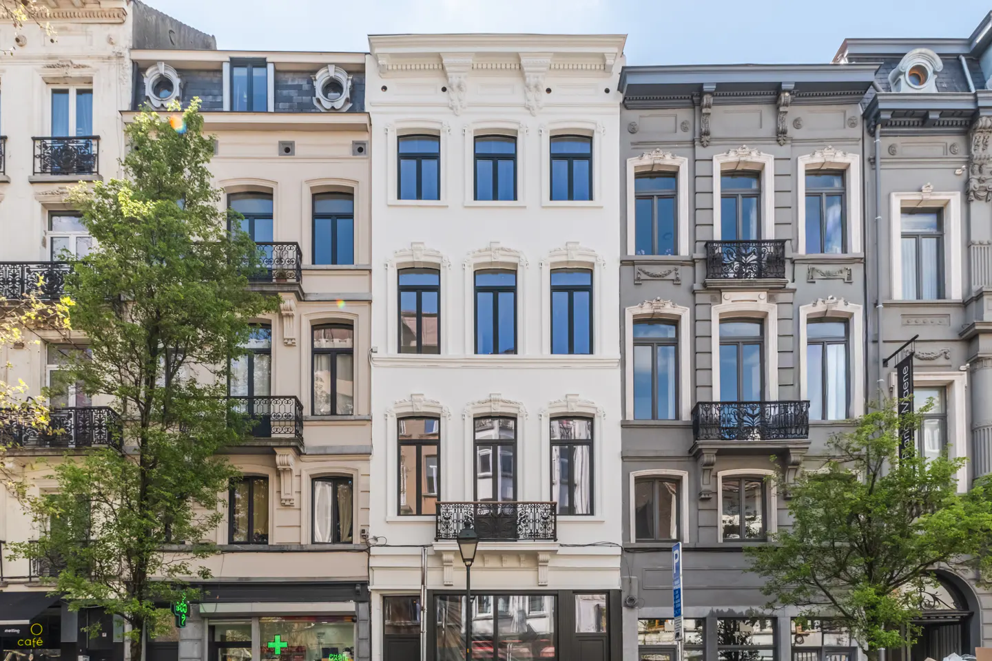 Row of multi-story buildings with ornate facades in varying colors, including white, beige, and gray, with dark windows and small balconies.