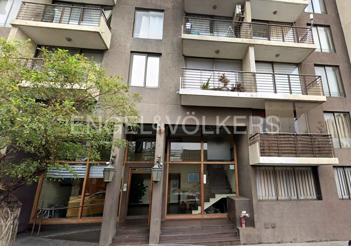 Exterior view of a gray apartment building with balconies and an Engel & Völkers real estate office on the ground floor.